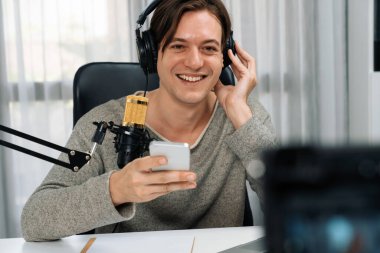 Akıllı yayıncının sunucu kanalı canlı sosyal medya yayını ile akıllı telefon kullanarak dinleyiciyle sohbet ediyor, kulaklık takarak modern ev stüdyosunda video kaydediyor. Bireysel.