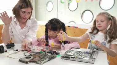 Yetenekli beyaz öğretmen öğrencilere dijital elektrikli aletleri öğretir ve açıklar. Uzman kız elektronik ekipman öğreniyor ve ana kartı cips ve kablolarla onarmak için kullanıyor. Etkinlik.