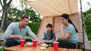 Aile hep birlikte bahçedeki kampta oturup yemek yiyor. Ebeveynler, genç nesil arasında iletişim kurmak ve zaman geçirmek için açık hava kamp faaliyetlerini kullanıyorlar. Uyumsuzluk.
