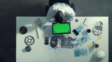 Türbin motoru veya jet motoru tasarımı ve çeşitli metal teçhizat dağılımı ile toplantı masasında yeşil ekranlı tablet üzerinde çalışırken telefona bakan mühendis görüntüsü. Hizalama.