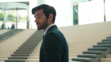 Akıllı iş adamı merdivenlerde kameraya bakıyor. İş elbisesi giyerken kameraya gülümseyen başarılı adamın yakın çekimi. Yönetici, kameraya bak. Hareket eden kamera. Sevinçli..