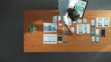 Yürüyen ve Ux Ui yazılımını yerleştiren yetenekli geliştiricilerin üst görünümü. Akıllı iş adamı toplantı masasına cep telefonu arayüzü ya da simgesi olan tablet koydu. Yatırımcı planı yazılım planı geliştirir. Cemaat.