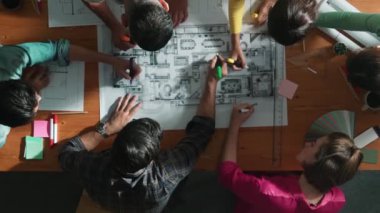İnşaat mühendisi ekibinin renkli paletlerle toplantı masasında yazı yazması. Yönetici proje planlarına bakarken bir grup farklı insan plan yapıyor ve not alıyor. Sempozyum.