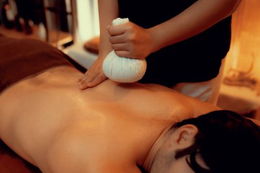 Sıcak bitkisel top spa masaj vücut tedavisi, masör erkek vücuduna nazikçe şifalı bitki torbası bastırıyor. Aromaterapi tesisinin sakinliği ve dinginliği kaplıca salonundaki mumların sıcacık ışığında. Sessiz.