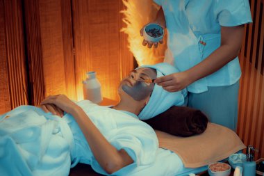 Kaplıca salonunun sakin atmosferi, kadın müşteri sıcak mum ve kömür kömürü yüz kremi masajıyla kendini yenileme zevkine kapılıyor. Yüz bakımı ve güzellik konsepti. Sessiz.