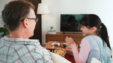 Büyükbaba ve torun televizyonda yemek izlemek için patates kızartması yiyorlar. Eski üst düzey kullanım teknolojisi, genç nesil çapraz nesil ile iletişim kurarak aile bağlarını güçlendiriyor. Uyumsuzluk.