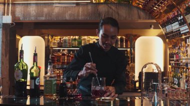 Zeki Asyalı barmen bardakta karıştırılmış alkol şurubunu buzla karıştırıyor. Çünkü kayanın üzerinde kamera var. Gece kulübünde taze kokteyl kokteylleri karıştırıyor. Vinosity.