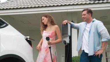EV şarj istasyonundan çevreci bilinci açık elektrikli araca sahip mutlu ve sevimli bir çift. EV araba teknolojisi gelecekteki sürdürülebilirlik için alternatif ulaşım aracı olarak kullanılıyor. Titiz