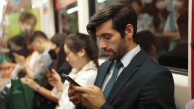 Gülümseyen beyaz iş adamı cep telefonuna bakıyor ya da trende otururken sosyal medya oynuyor. Çekici proje yöneticisi yoğun saatlerde toplu taşıma araçlarını kullanarak iş yerine gidiyor. Sevinçli..
