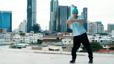 Beyaz tenli dansçı çocuk çatıda sokak dansı yapıyor şehir siteleriyle ya da şehirlerle. Genç adamın sokak dansı yaparken dondurucu poz vermesi. Açık hava sporu 2024. Hiphop.