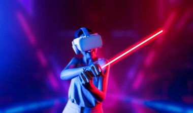 VR kulaklık takan zeki bir kadın metaevrene bağlanıyor, gelecekteki siber uzay topluluğu teknolojisi. Kılıç dövüşü oynarken lazer kılıcını sıkıca tutan zarif bir kadın. Halüsinasyon.