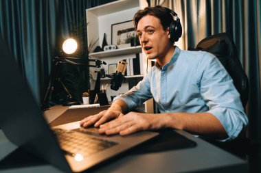 Sunucu kanalı akıllı yayıncı laptopta canlı sosyal medya uygulaması arıyor, kulaklık takıyor ve modern ofis stüdyosundaki mikrofonu kullanıyor. Bireysel.