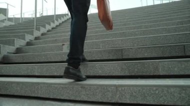 Akıllı bir iş adamının elinde çantayla merdivenlerden yukarı çıkışının en üst görüntüsü. Profesyonel proje yöneticisi merdivenlerden çıkıp işyerine gidiyor. Yeteneklerini arttırmak, terfi almak, seyahat etmek. Sevinçli..
