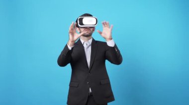 İş adamı artırılmış gerçeklik teknolojisi kullanarak veri yönetiyor. Kafkasyalı yatırımcı VR gözlük takıyor ve mavi arka planda dururken pazarlama stratejisi planlıyor. Aygıt.
