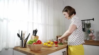 Enerjik anne, mutfak malzemeleri ile çevrili sebzeleri doğrarken modern mutfakta kahvaltı için salata yapıyor. Akıllı kadın temizlikçi yemek pişirir ve yemek hazırlar. Sağlıklı bir yaşam tarzı. Pedagoji.