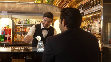 Akıllı barmen, lüks bir tezgahta arkadaşını beklerken limonlu cin kokteyli ikram ediyor. Barmen, canlı gece hayatı parti atmosferinde mükemmel hizmet veriyor. Vinosity.