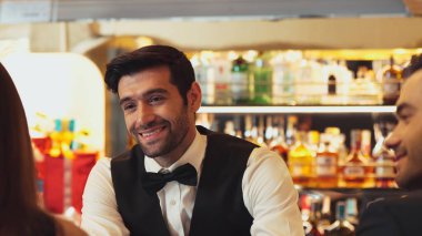 Güzel görünümlü barmen, içki tezgahındaki çiftle samimi bir gülümseme sohbeti yaparken aynı zamanda hoş geldin içkisi ve özel menü listesi öneren çekici profesyonellik. Vinosity.