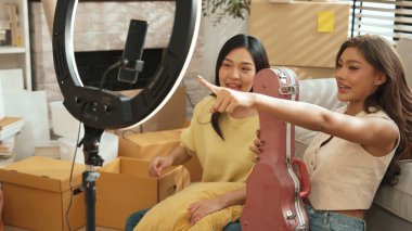 İnternette yayınlanırken gitar kılıfını gösteren ve satan mutlu bir çift. Çekici kız oturma odasında reklam ürünleri için online pazarlama kullanarak yayın yapıyor. Myrmidon.