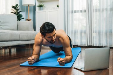 Atletik ve sporcu adam, evdeki formda fiziğe ve sağlıklı spor yaşam tarzına uygun vücut egzersizi sırasında spor minderinde kalas yapıyor. Gaiety evde egzersiz eğitimi.