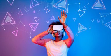 VR gözlüklü Afrikalı kız mavi ve pembe arka planda duruyor ve yüzen geometrik şekle bakıyor. Heyecanlı insan görsel gerçeklik dünyasına giriyor. Teknoloji yeniliği. Yaratıcılık.