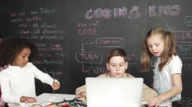 Kafkasyalı çocuk dizüstü bilgisayar programlama kodunu ve yazma programını kullanırken bir grup farklı çocuk BTMM teknoloji sınıfında kontrolörlük yapıyor ve hemen karatahtayla yazılmış. Etkinlik.