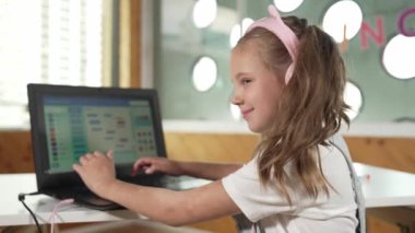 Gülümseyen kız program sistemi ya da STEM teknoloji eğitiminde kodlama programı. Laptop yazma kodunu kullanarak çalışırken kulaklık takan bir çocuk kameraya bakmak için arkasını döner. Etkinlik.