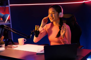 Geceleri podcast 'te olumlu konuşmalar yapan, pembe neon ışıklı modern stüdyoda sunum için dizüstü bilgisayar kullanan, gülümseyen, genç, güzel Asyalı bir etkileyiciydi. Taktik.