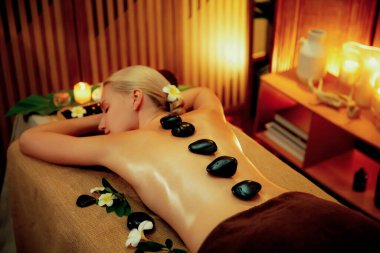 Lüks tatil köyündeki kaplıcalarda sıcak taş masajı, sıcak mum ışığı, spa bazalt taşı masajının keyfini çıkaran mutlu kadın müşteriler, rahatlatıcı bir sıcaklıkla vücudun üzerinde süzülüyorlar. Sessiz.