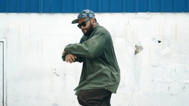 Sokak ortasında mavi duvarlı hippi dansçı ayak basamağı. Asyalı break dansçı kollarını açarken sokak dansı yapıyor. Hip hop koreografı enerjik bir dans sergiliyor. Açık hava sporu 2024 hiphop..