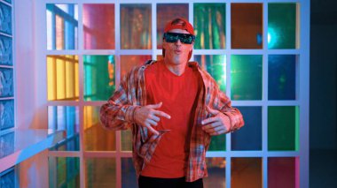 Komik break dansçı kameraya bakarken hiphop 'a doğru serbest adım atıyor. Çılgın mutlu hipster dans edip sokak dansı yaparken Led ışığında günlük kıyafet ve güneş gözlüğü takıyor. Mutluluk.