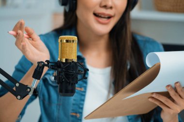 Sosyal medyada kulaklıkla canlı yayın yapan Asyalı sunucu modern stüdyoda yaşam koçluğu veya pazarlama dinleyicilerini selamlıyor. Taktik.