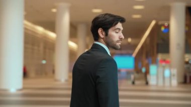 Profesyonel bir iş adamı kolları bağlıyken arkasını döner. Kafkasyalı mutlu yatırımcı, arka planı bulanık bir şekilde koridorda kollarını kavuştururken kameraya özgüvenle bakıyor. Portre. Sevinçli..