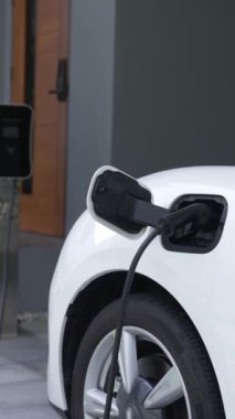Adamın biri evinde elektrikli araç şarj aletinin fişini çekiyor. İlerici bir yaşam tarzında elektrikli araçların kullanımı, temiz ve sağlıklı bir çevreye katkıda bulunur..