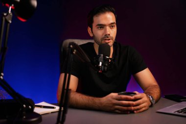 Yayıncı elinde kahve fincanıyla hayran kulübü dinleyicisiyle konuşuyor, canlı yayında neon ışık stüdyosundaki yaratıcı pozitif düşünce konseptiyle ilgili finansal sorunları tartışıyor. Tahmin et..