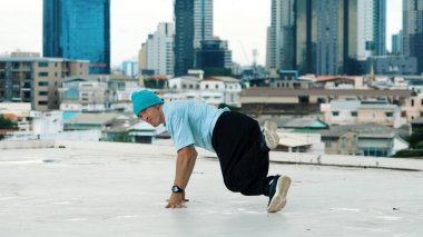 Beyaz tenli dansçı çocuk çatıda sokak dansı yapıyor şehir siteleriyle ya da şehirlerle. Genç adamın sokak dansı yaparken dondurucu poz vermesi. Açık hava sporu 2024. Hiphop.