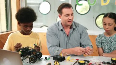 Akıllı akıl hocası araba modelini tamir ederken elektronik aletleri öğretiyor. Kafkas öğretmeni masadaki dizüstü bilgisayarlı robot inşaatı açıklarken, araba modeli etrafa saçılmış. Öğretim