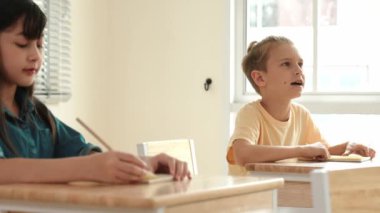 Zeki öğrenci sınıfta otururken öğretmenlerin sorularına cevap verir. Tahtaya bakarak ve ilköğretim sınıfına katılarak çeşitli çocuklar öğreniyor ve öğreniyor. Eğitim konsepti. Pedagoji.