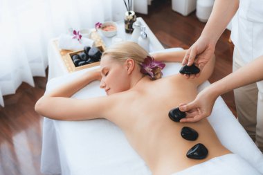 Lüks tatil köyündeki kaplıcalarda sıcak taş masajı. Gün ışığı sükunet ortamında, mutlu kadın müşteri bazalt taş masajından zevk alıyor. Rahatlatıcı bir sıcaklıkla vücudun üzerinde süzülüyor. Sessiz.