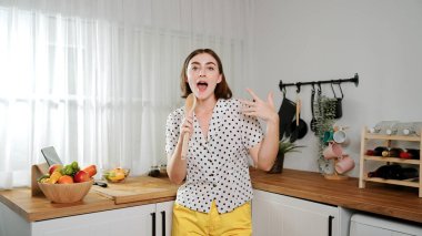 Enerjik beyaz anne kahvaltı için salata pişirirken ve yemek pişirirken elinde kepçeyle şarkı söylüyor. Sağlıklı yemek yapmaya hazırlanırken müziğe yönelen mutlu ev sahibi. Pedagoji.