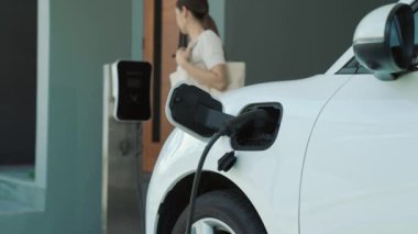 Bir kadın evinde elektrikli araç şarj aletinin fişini çekiyor. İlerici bir yaşam tarzında elektrikli araçların kullanımı, temiz ve sağlıklı bir çevreye katkıda bulunur..