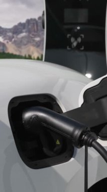 Temiz çevre için temiz enerjinin yol açtığı ilerici elektrikli araba kavramının arka planı olarak dağın tepesinde bulutun zaman kavramının yer aldığı doğal manzara. EV araba şarj istasyonunda şarj oluyor..