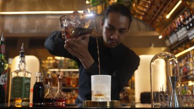 Asyalı barmen soğuk bardağa karışık viski dökerek soğutmalı buzlu içecek üretiyor. Lüks ılık barlarda alkol yenileme gösterisine odaklanan yaratıcı bir reklam yapıyor. Vinosity.