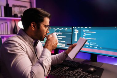 Akıllı bilişim geliştiricisi, bilgisayar ekranındaki yazılım geliştirme kodlaması üzerine kahveyle birlikte çalışıyor, en yeni uygulama projesi programı ile birlikte neon ışıklı siber ofiste çevrimiçi web sitesi verilerini güncelliyor. Tahmin et..