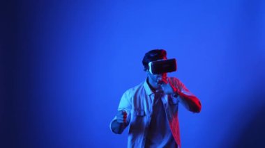 Sanal dünyada kılıç ve eskrim yaparken VR gözlük takan zeki bir oyuncu. Çekici erkek model, mavi arka planda dikilirken ve metaevrene erişirken aksiyon oyunu oynuyor. Aygıt.