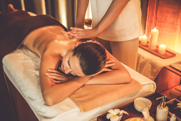 Caucasian woman customer enjoying relaxing anti-stress spa massage and pampering with beauty skin recreation leisure in warm candle lighting ambient salon spa at luxury resort or hotel. Quiescent