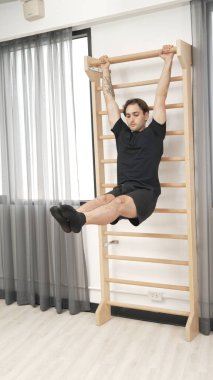 Asılı bacak egzersizi yapan mutlu bir adam vücut kaslarını güçlendirmek ve beden eğitimini iyileştirmek için duvar parmaklıkları üzerinde egzersiz yapıyor. Alt karın bölgesini iyileştirmek için erkek antrenör bacak yükseltme ameliyatı. Alışkanlık.