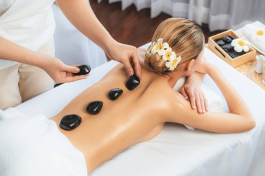 Lüks tatil köyündeki kaplıcalarda sıcak taş masajı. Gün ışığı sükunet ortamında, mutlu kadın müşteri bazalt taş masajından zevk alıyor. Rahatlatıcı bir sıcaklıkla vücudun üzerinde süzülüyor. Sessiz.