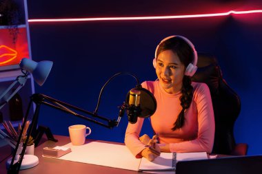 Geceleri podcast 'te olumlu konuşmalar yapan, pembe neon ışıklı modern stüdyoda sunum için dizüstü bilgisayar kullanan, gülümseyen, genç, güzel Asyalı bir etkileyiciydi. Taktik.