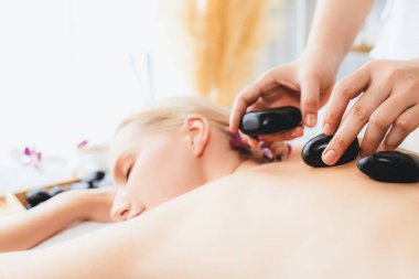 Lüks tatil köyündeki kaplıcalarda sıcak taş masajı. Gün ışığı sükunet ortamında, mutlu kadın müşteri bazalt taş masajından zevk alıyor. Rahatlatıcı bir sıcaklıkla vücudun üzerinde süzülüyor. Sessiz.