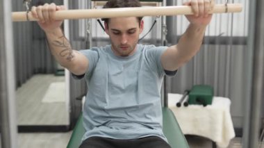 Adam spor salonundaki kol ve vücut kaslarını güçlendirmek için pilates trapez çubuğunda çekirdek egzersizi yapıyor. Göğüs ve omuz güçlendirmek için Cadillac 'a göğüs presi yapan antrenör. Alışkanlık.